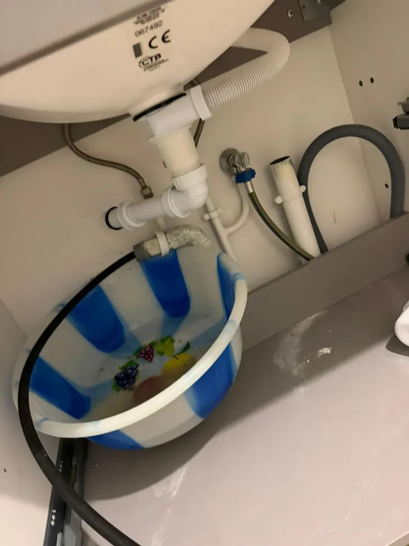 Fuite sous un évier avec siphon démonté et bassine de récupération